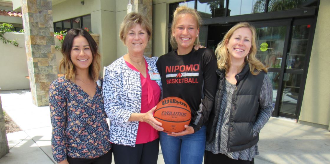 Four young ladies holding a basketball and smiling